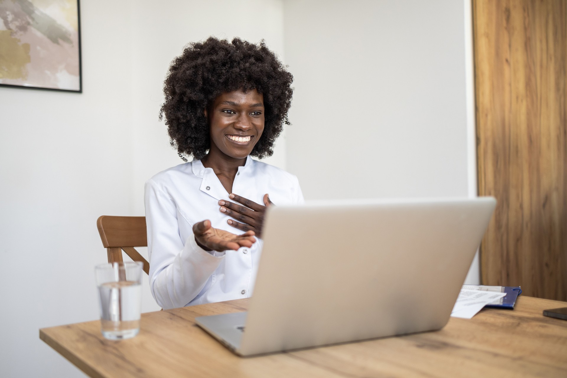 A young black female doctor conducting online consultations with patients via video call from her home office.